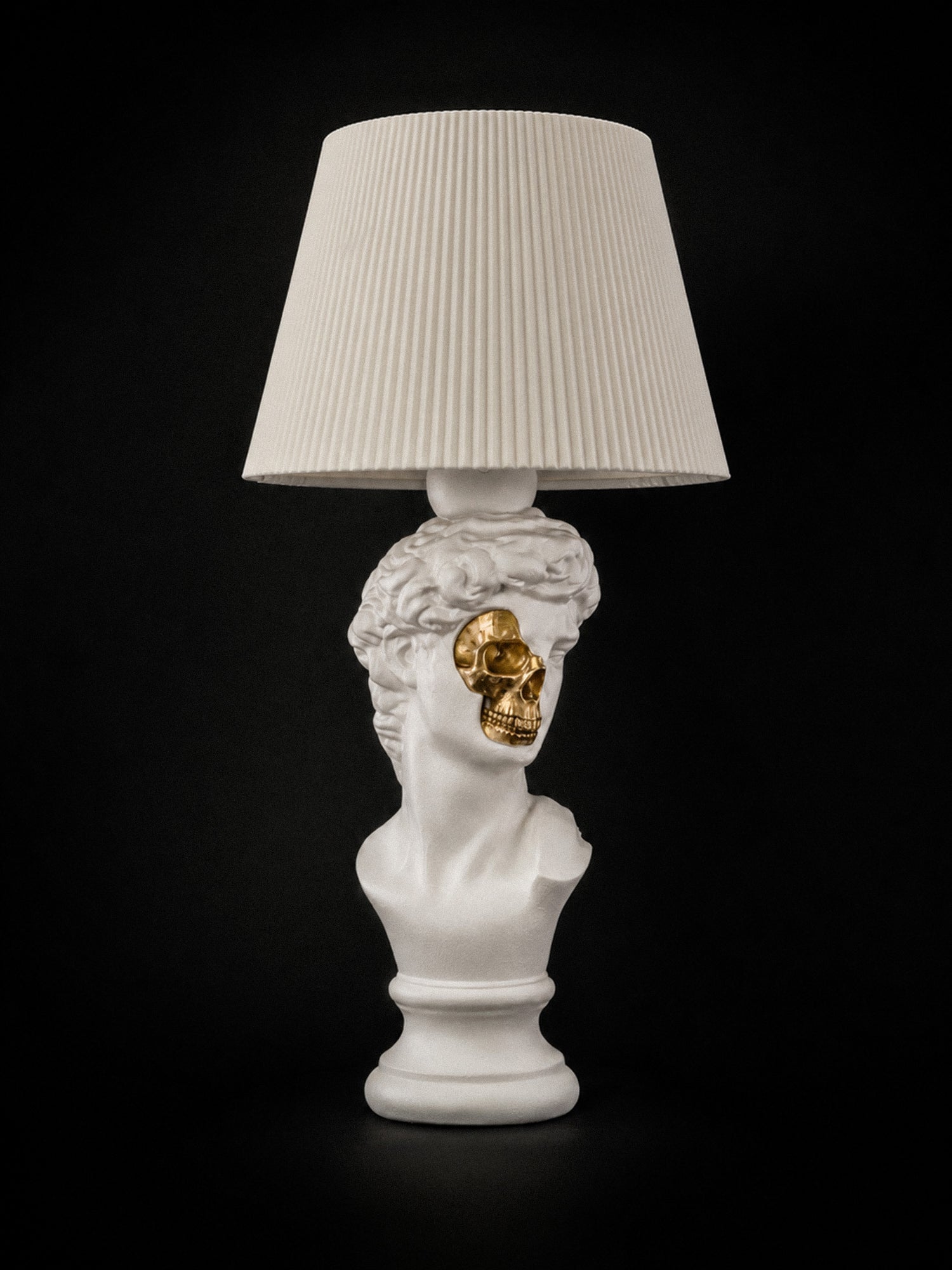 White David sculptural lamp with exposed metallic-gold skull and white pleated shade