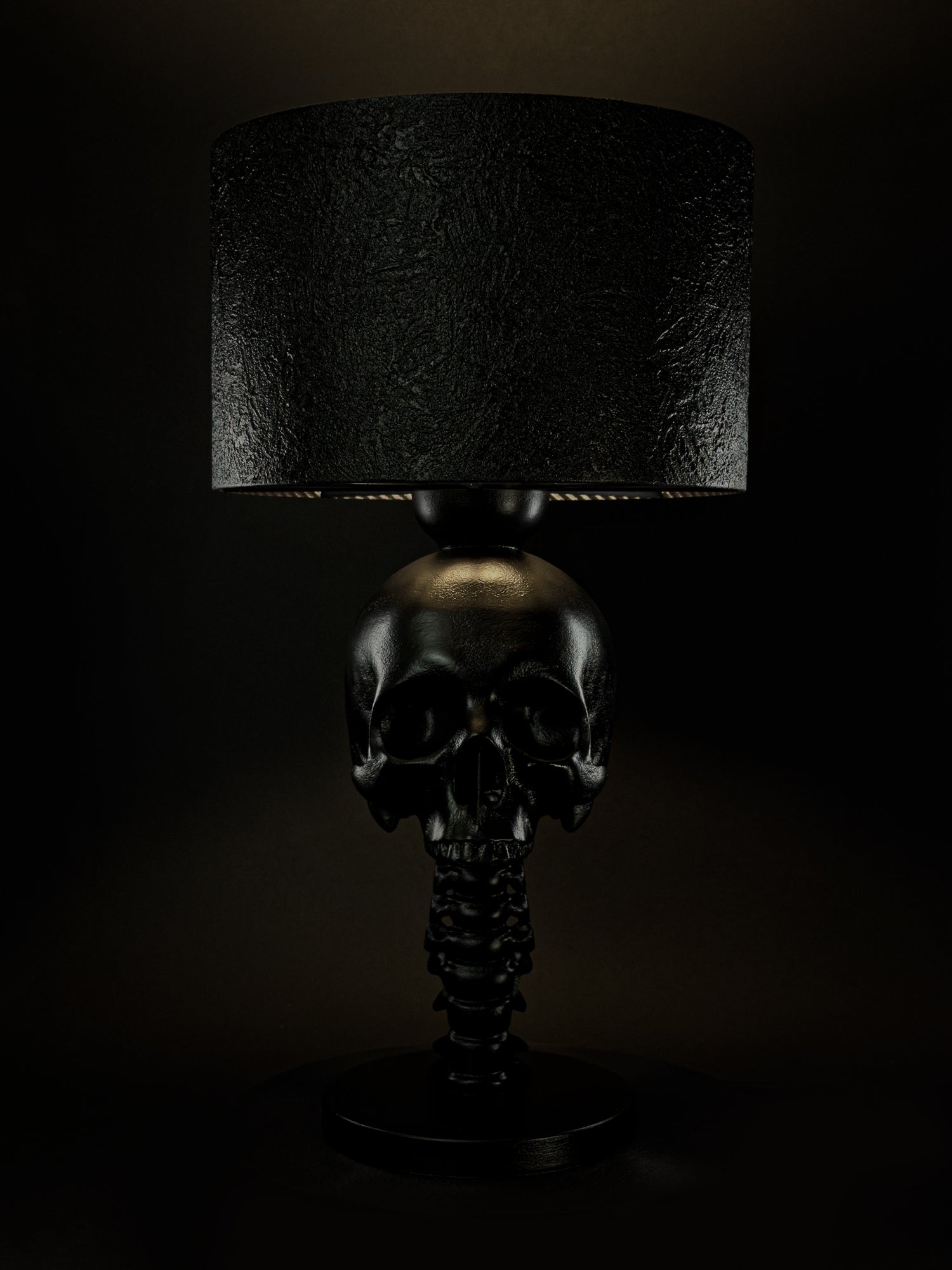Illuminated Skull Spine table lamp shown from the front with a black textured lampshade