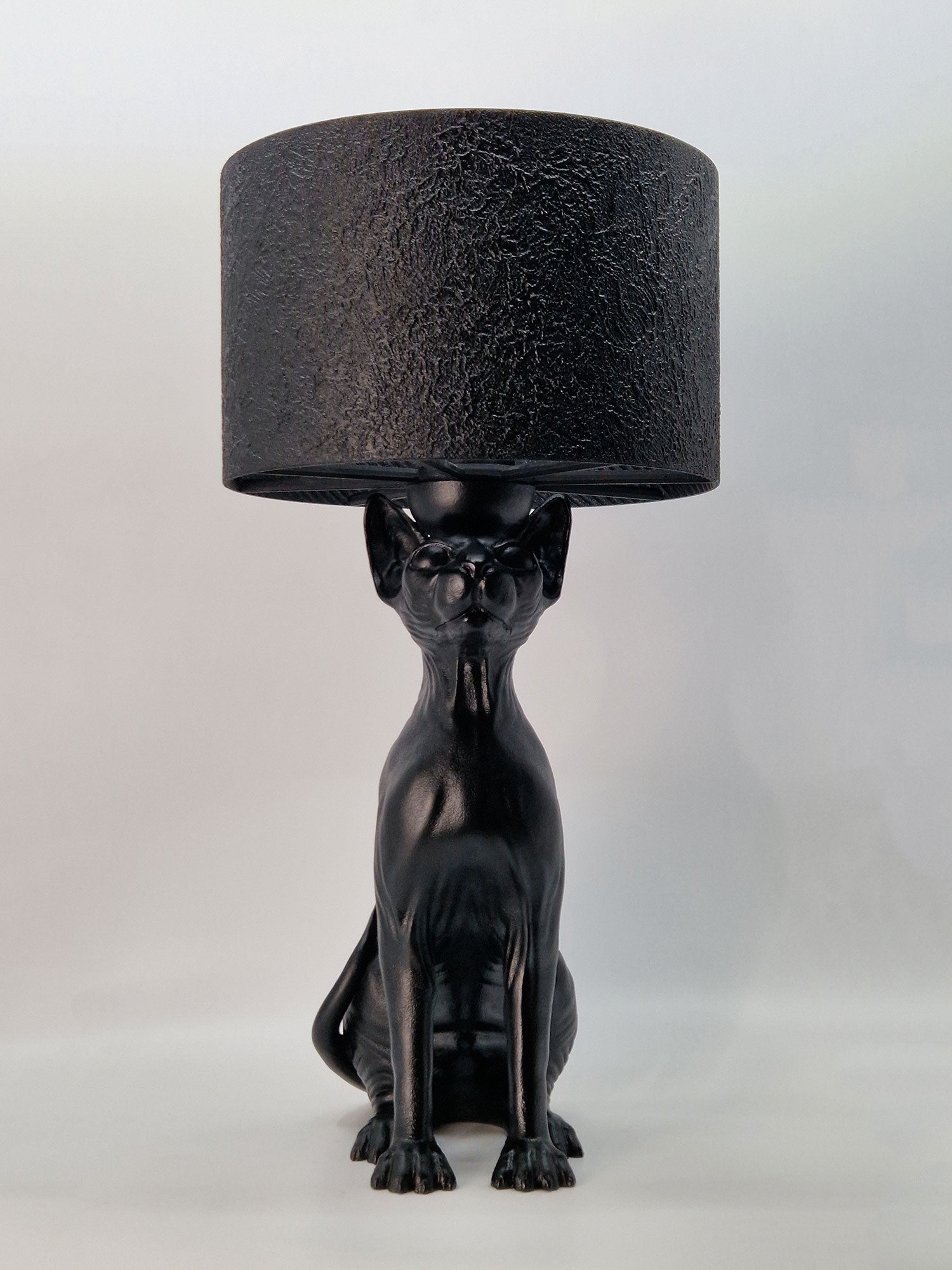 Front view of a hairless Sphynx cat sculpture lamp in matte black, showcasing anatomical skin details.