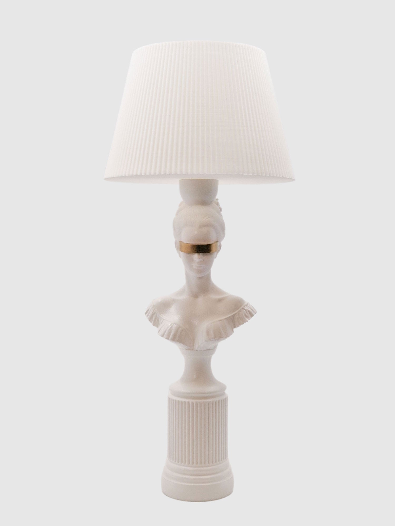Front view of the Blind Hera lamp in white with a metallic gold blindfold and pleated white lampshade.