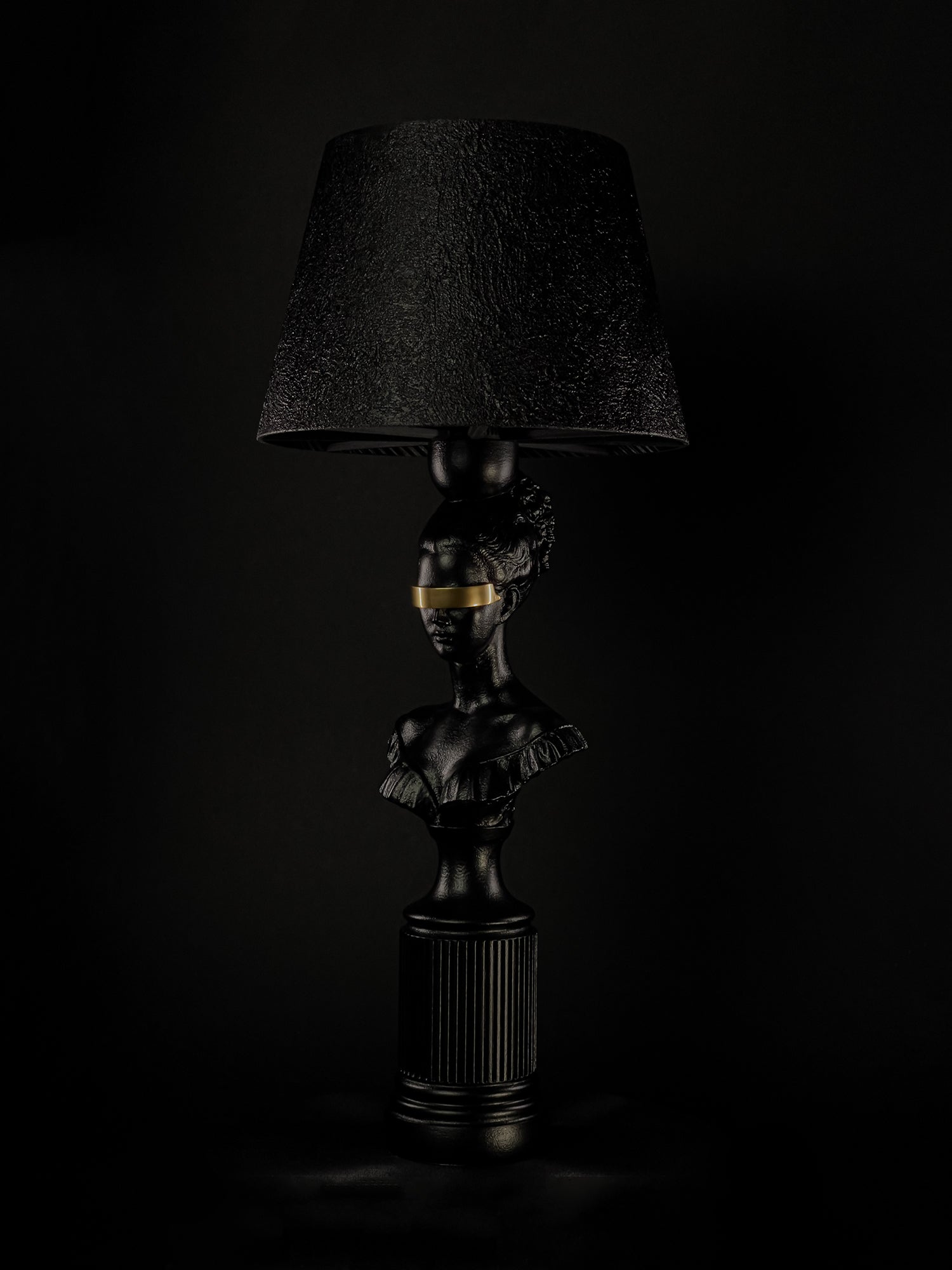 Front view of the satin-black Blind Hera bust lamp with gold blindfold and textured shade