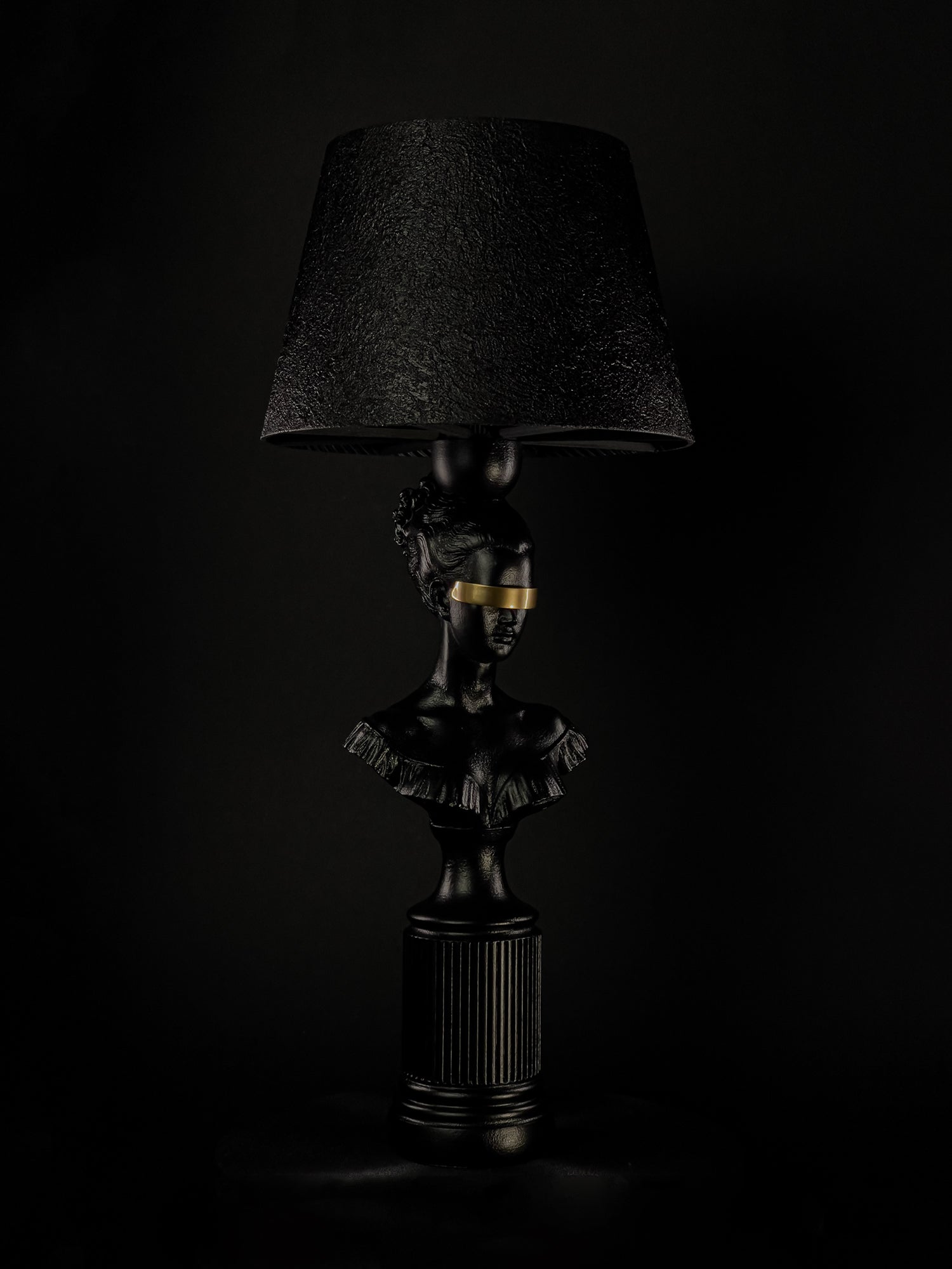 Side view of the Blind Hera classical bust lamp with a metallic-gold blindfold