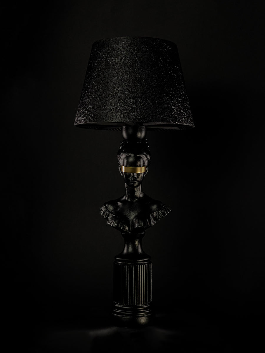 Blind Hera sculptural lamp in satin black with a metallic-gold blindfold, shown from a three-quarter angle