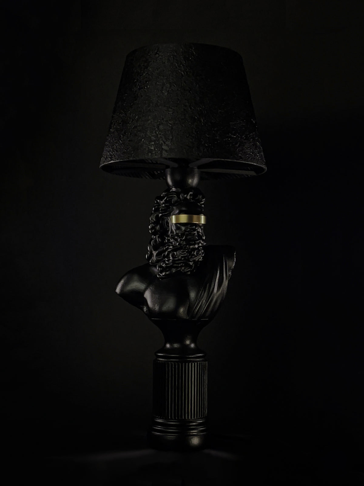 Three-quarter view of the satin-black Blind Zeus bust lamp with metallic-gold blindfold