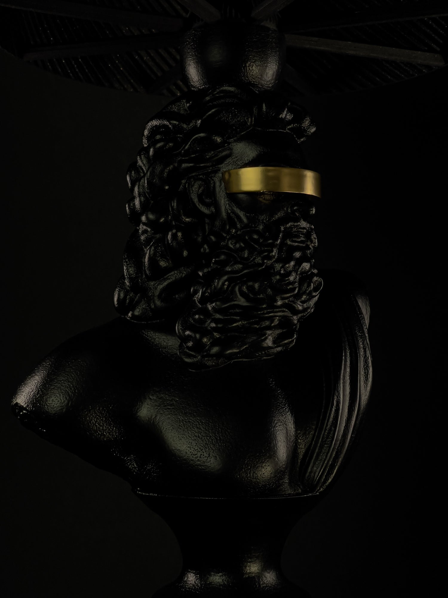 Close-up of Blind Zeus’s bearded classical bust and gold blindfold