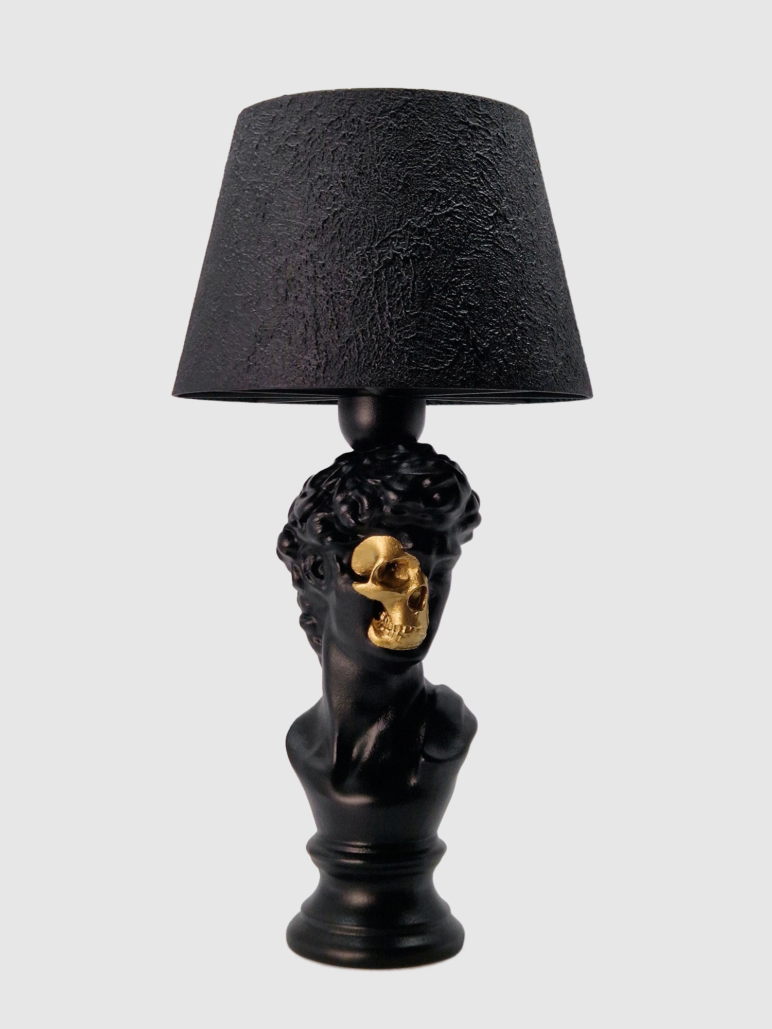 Front view of the David bust lamp in matte black featuring a gold-plated half-skull face and black shade, original Horror Romance design.