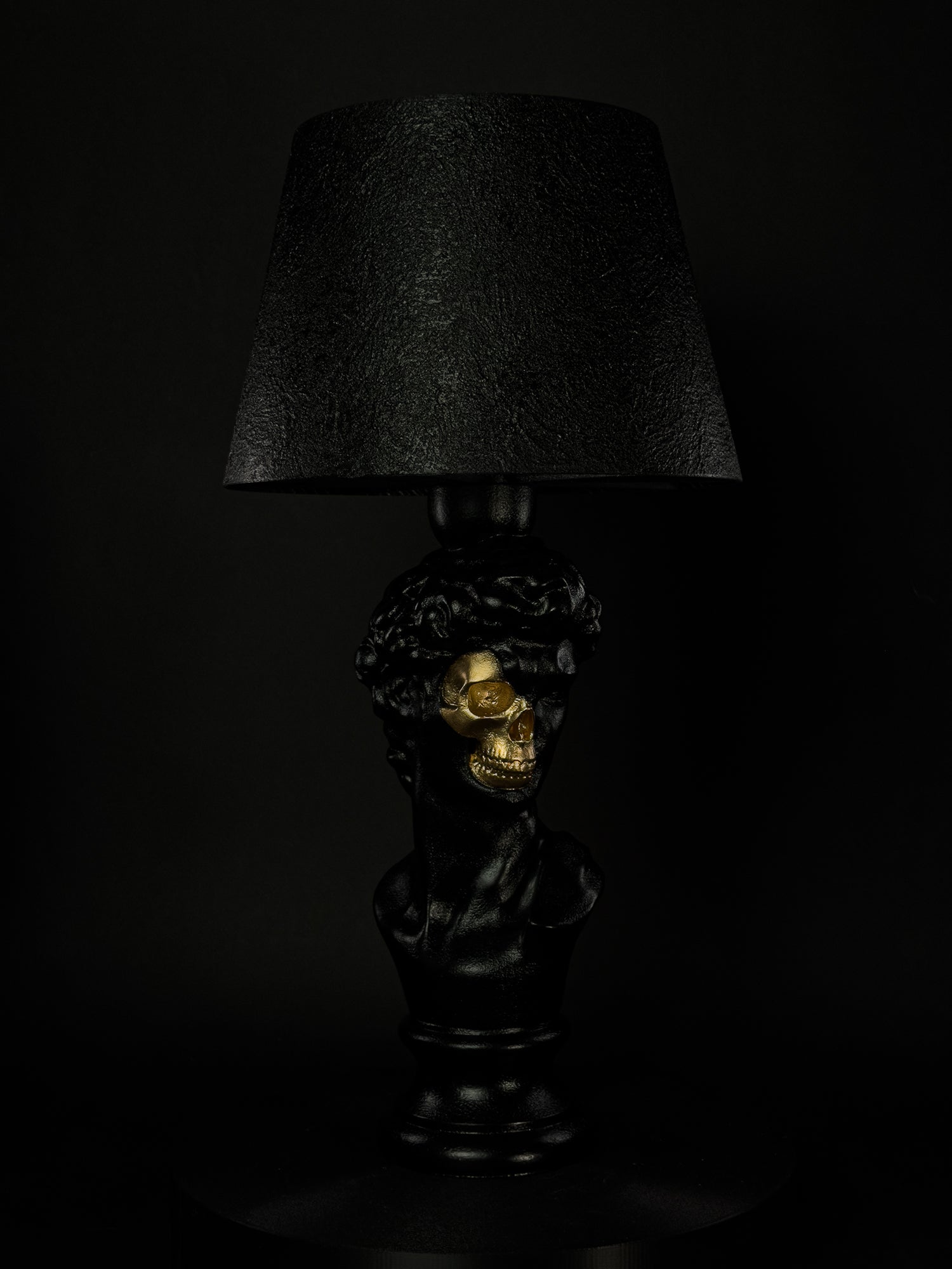 David sculptural lamp in satin black with exposed gold skull, shown from a three-quarter angle