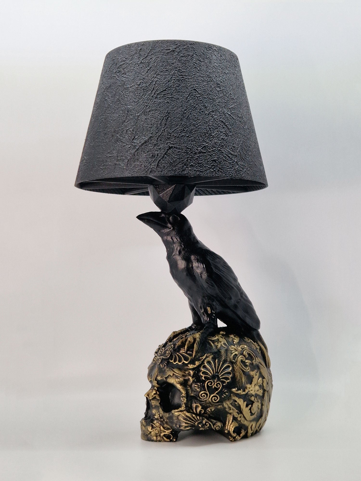 Angled view of the raven lamp base highlighting the metallic gold filigree and anatomical raven details.