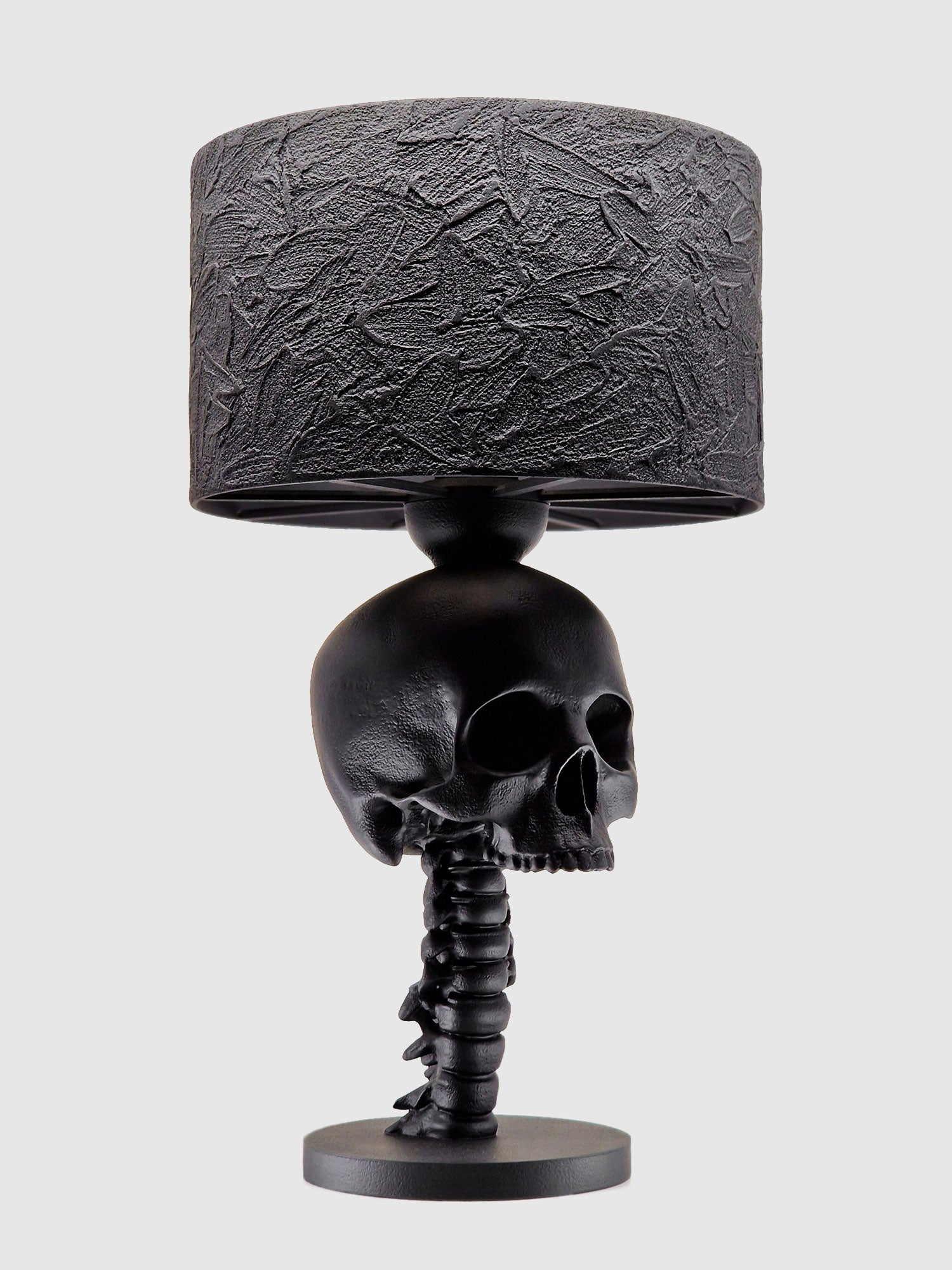 Angled profile view of the black Skull Spine desk lamp showing the detailed anatomical cervical spine column, original Horror Romance design.
