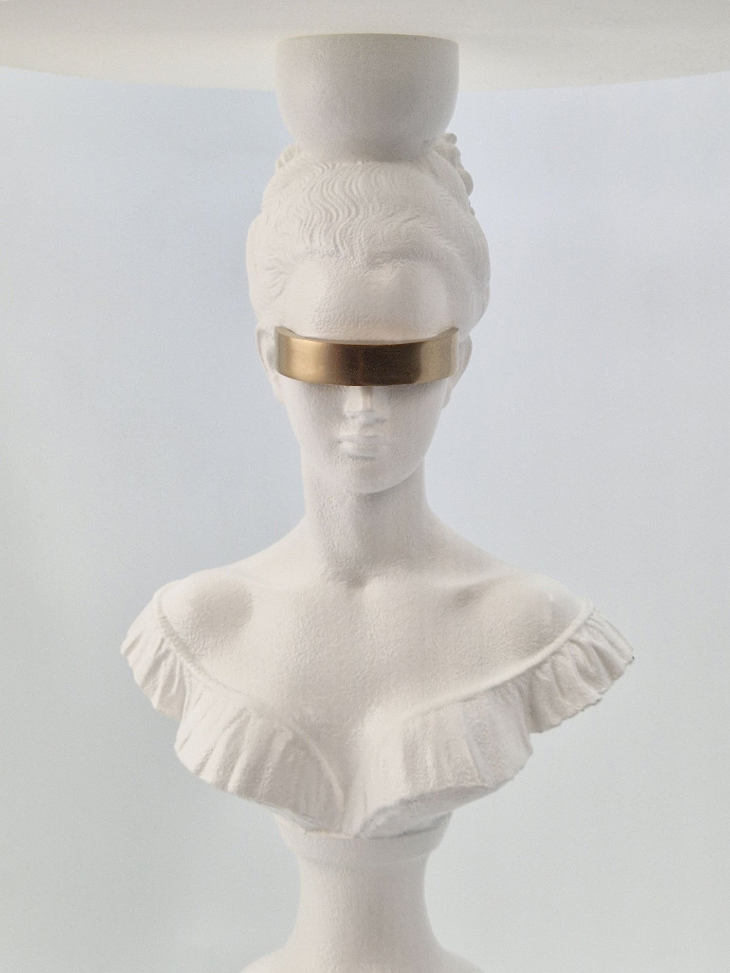 Extreme close-up of the Hera lamp's gold-plated blindfold and intricate neoclassical facial features.