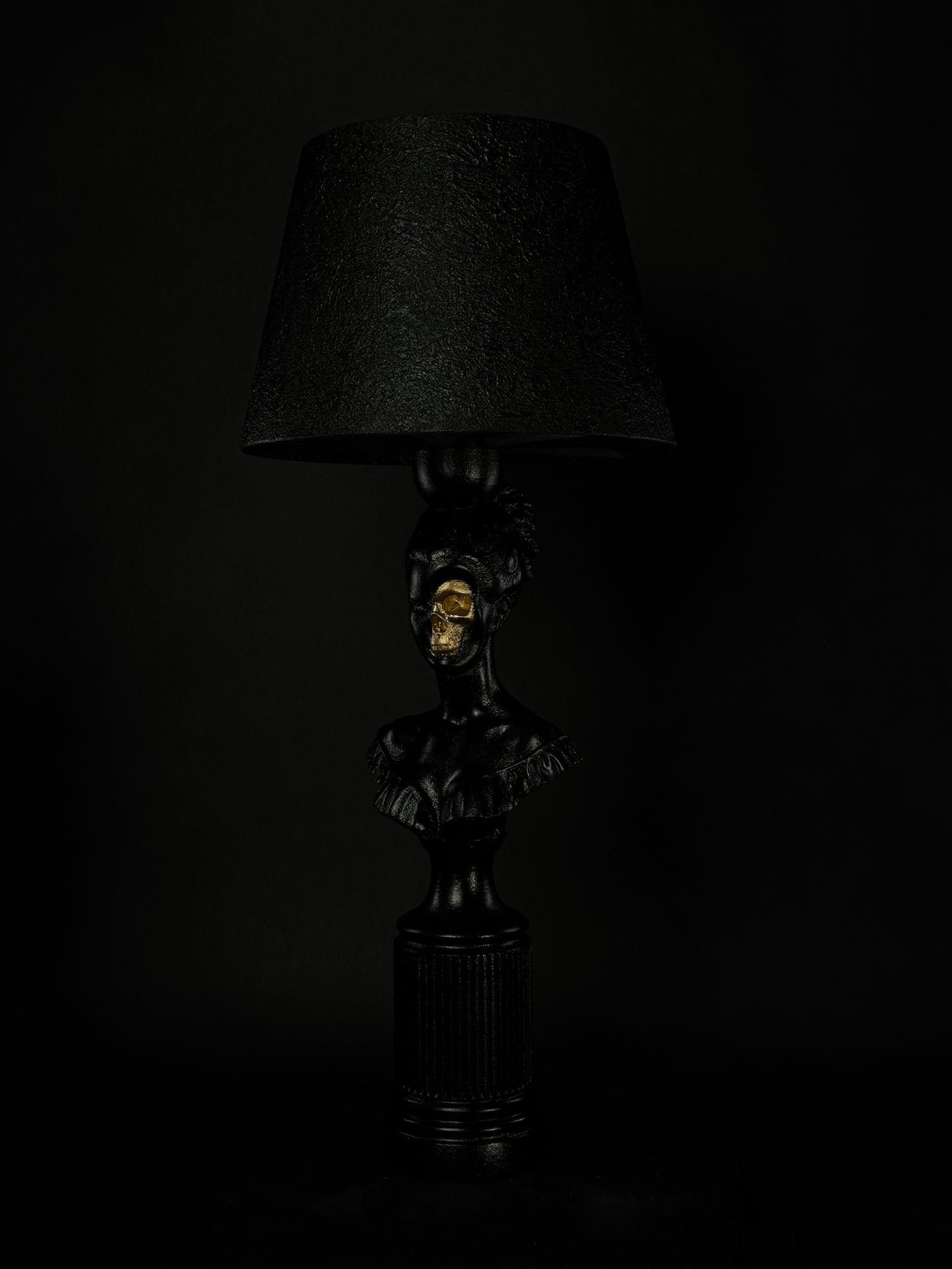 Three-quarter view of the satin-black Hera sculptural lamp with exposed metallic-gold skull