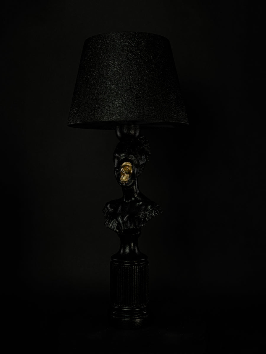 Three-quarter view of the satin-black Hera sculptural lamp with exposed metallic-gold skull
