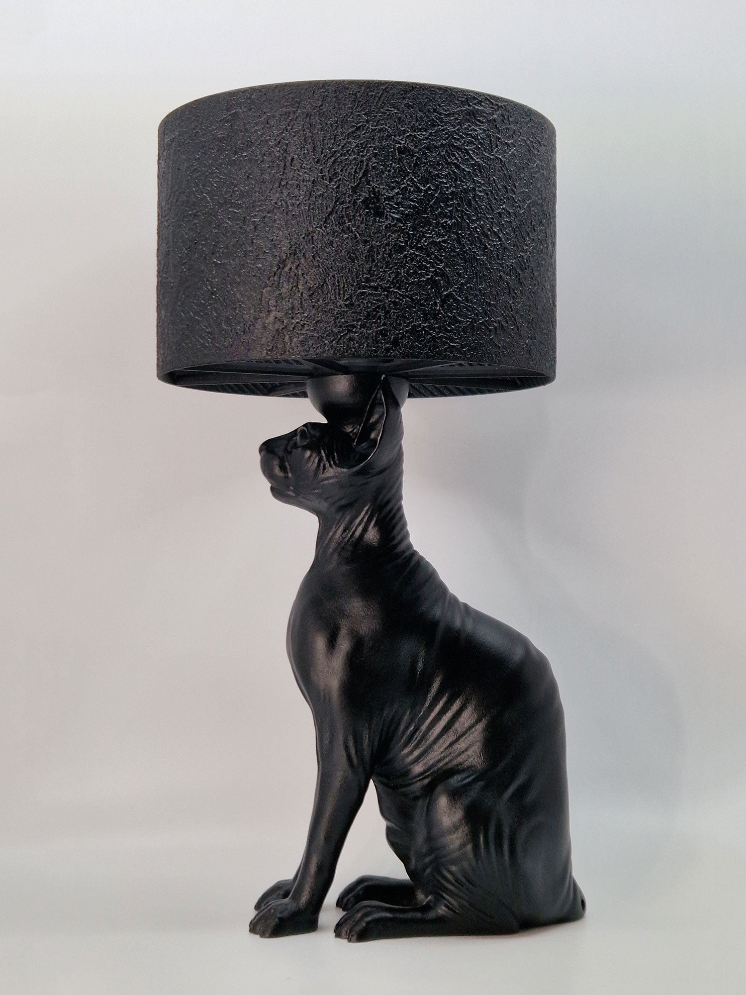 Lifestyle shot of the black Sphynx cat lamp on a marble console table in a dark green room with gold accents.