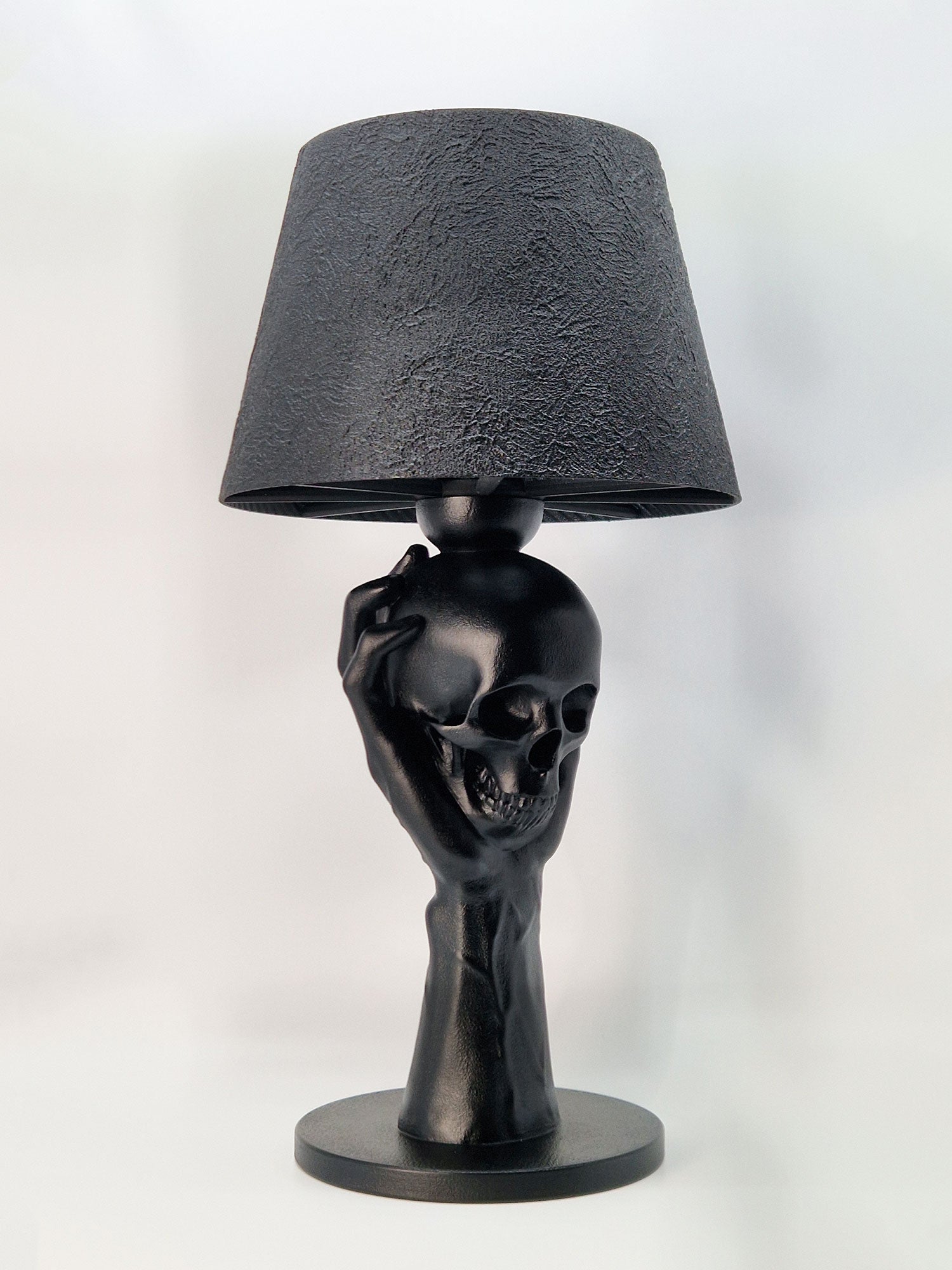 Close-up angled view of the skull and hand lamp base, showcasing the matte black finish and realistic bone textures.