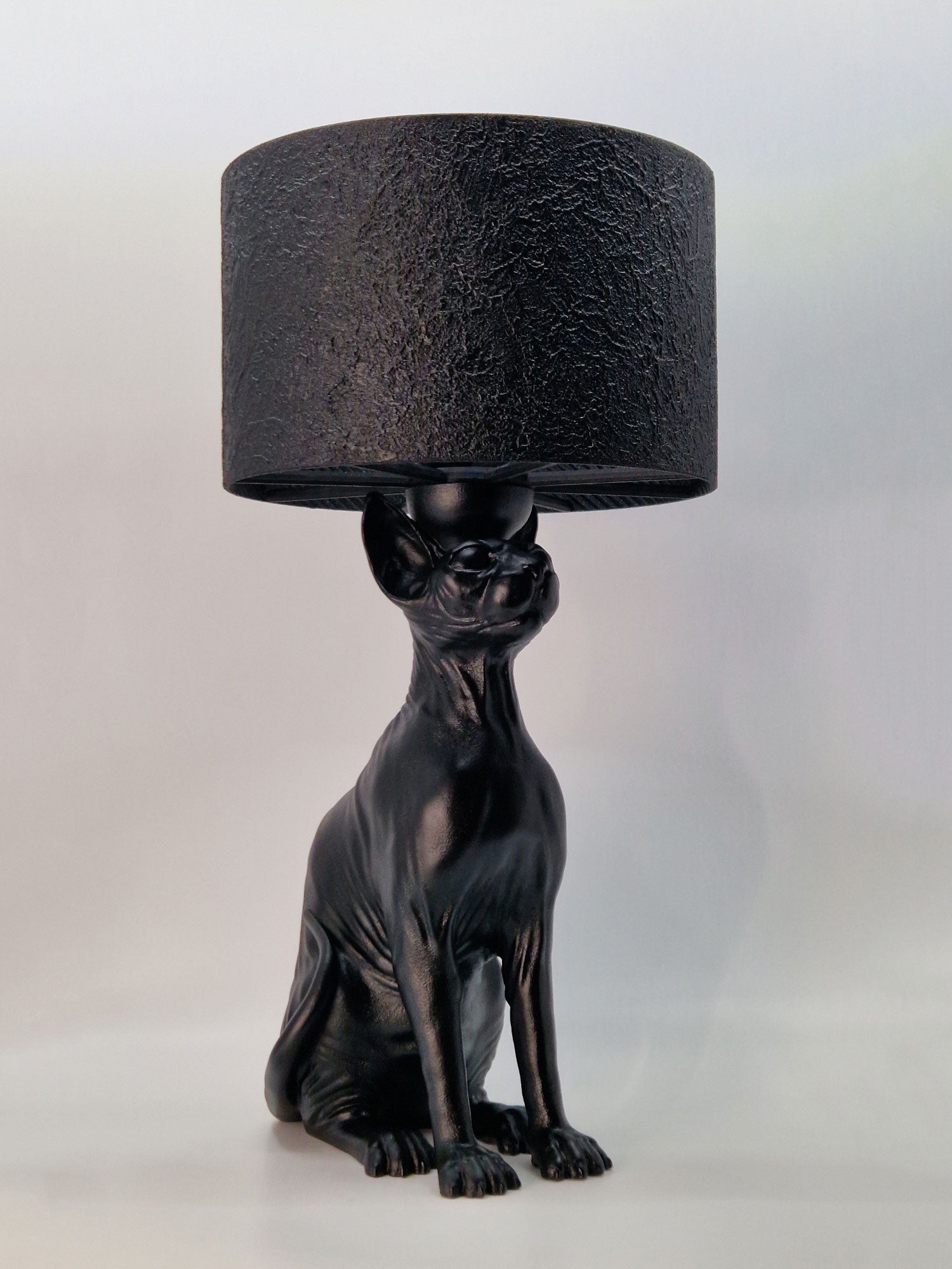 Angled front view of the Purrfect Lamp, a black hairless cat sculpture used as a decorative lamp base.