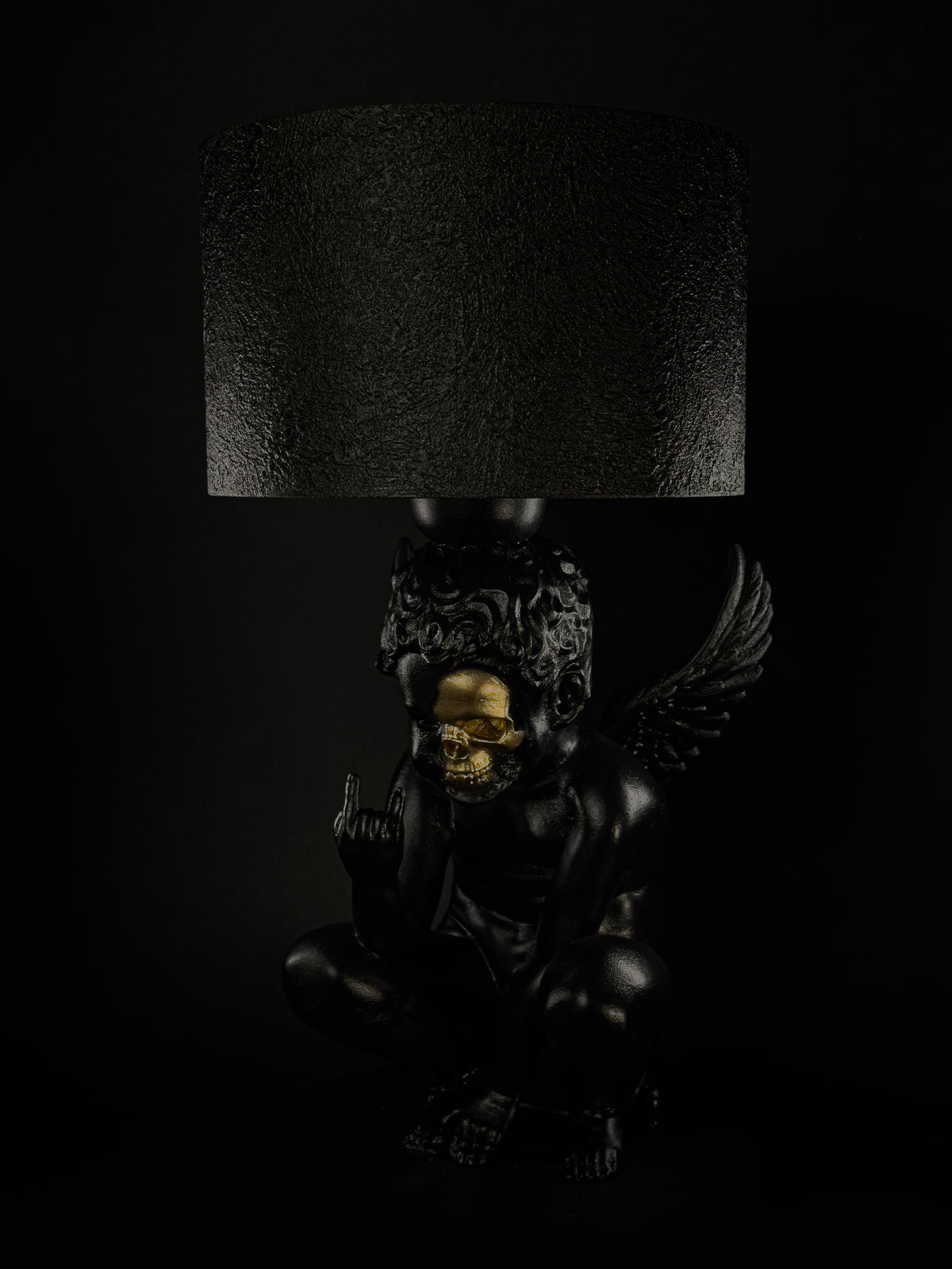 Three-quarter view of Rebel Angel lamp showing the cherub's gold half-skull face and raised hand gesture.