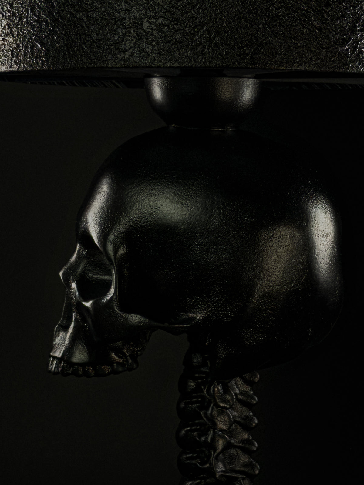 Side close-up of the black skull, vertebrae, and sculpted surface of the Skull Spine lamp