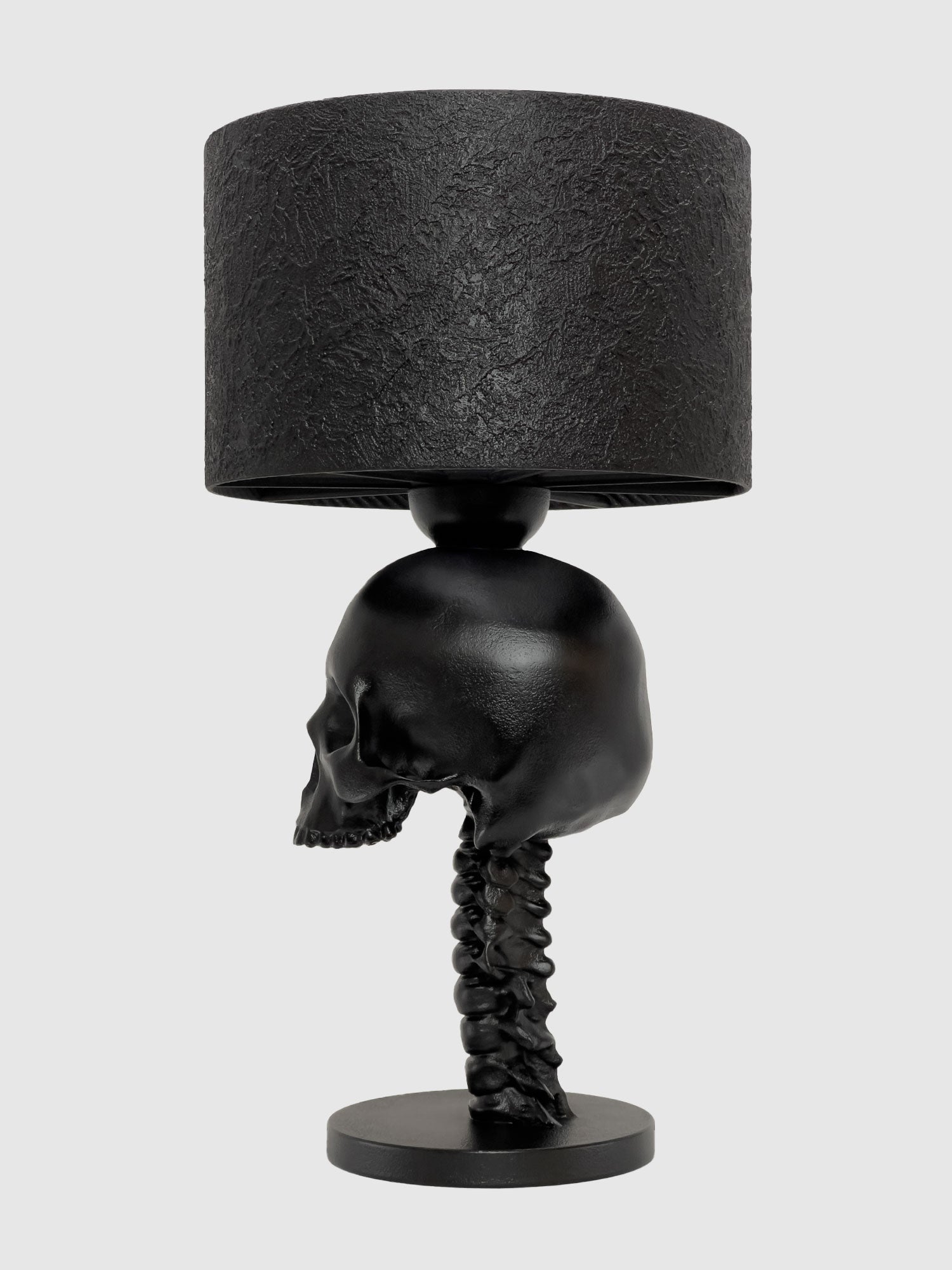 A left-side profile of the gothic skull lamp. The monochromatic black pigment and mineral-concrete coating highlight the anatomical accuracy of the jawline and cervical spine against a neutral background, designed and manufactured by Horror Romance.