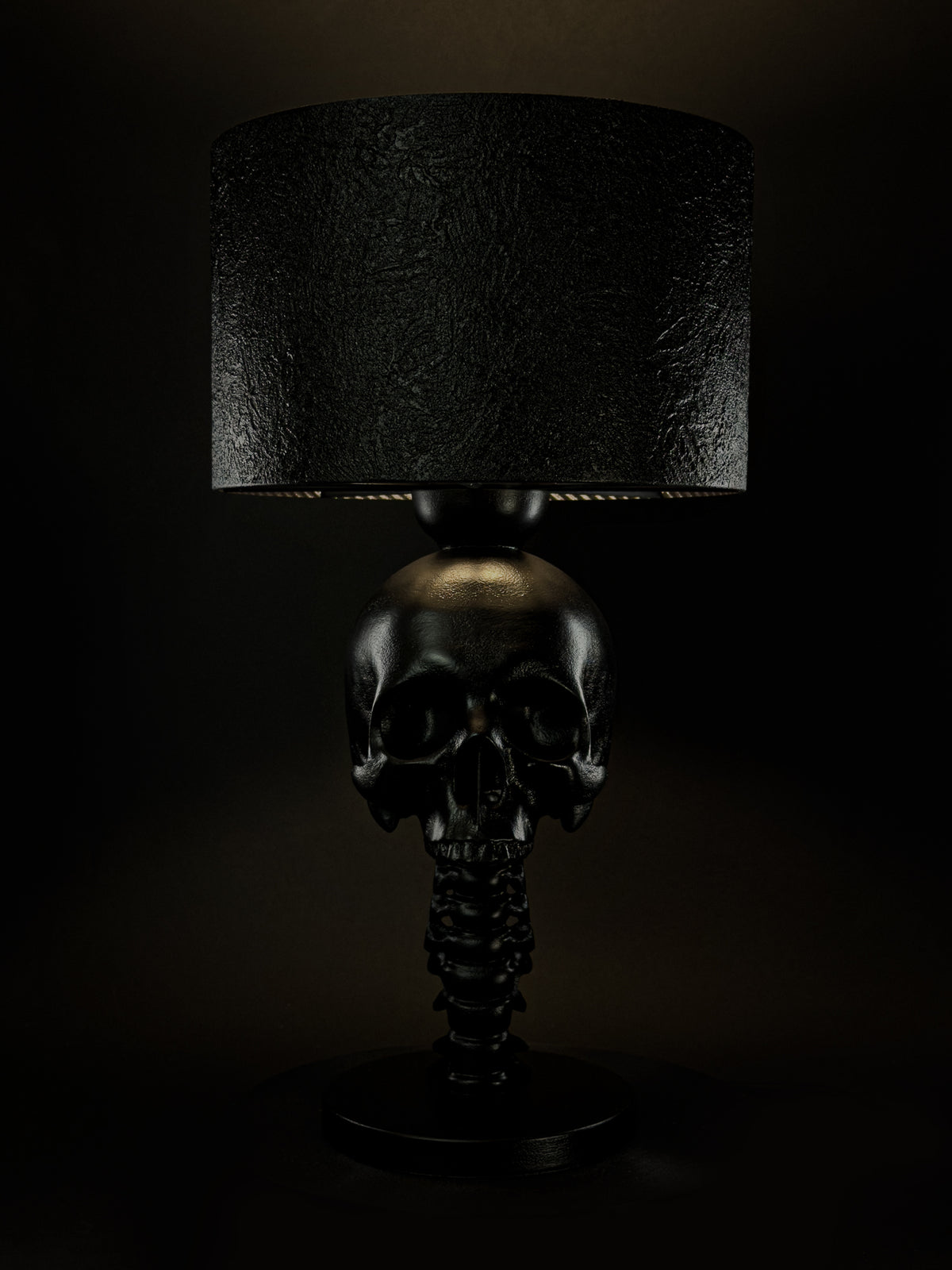Illuminated Skull Spine table lamp shown from the front with a black textured lampshade