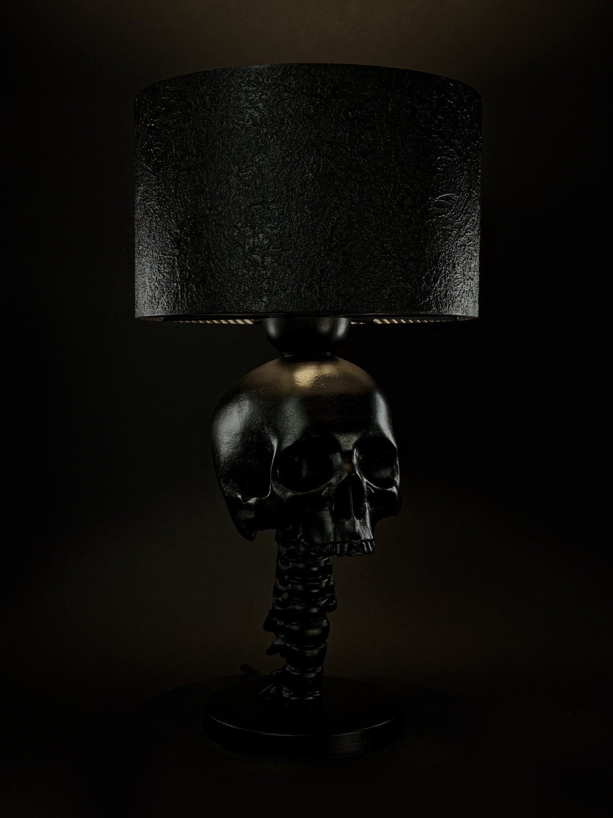 Illuminated black Skull Spine sculptural lamp shown from a three-quarter side angle