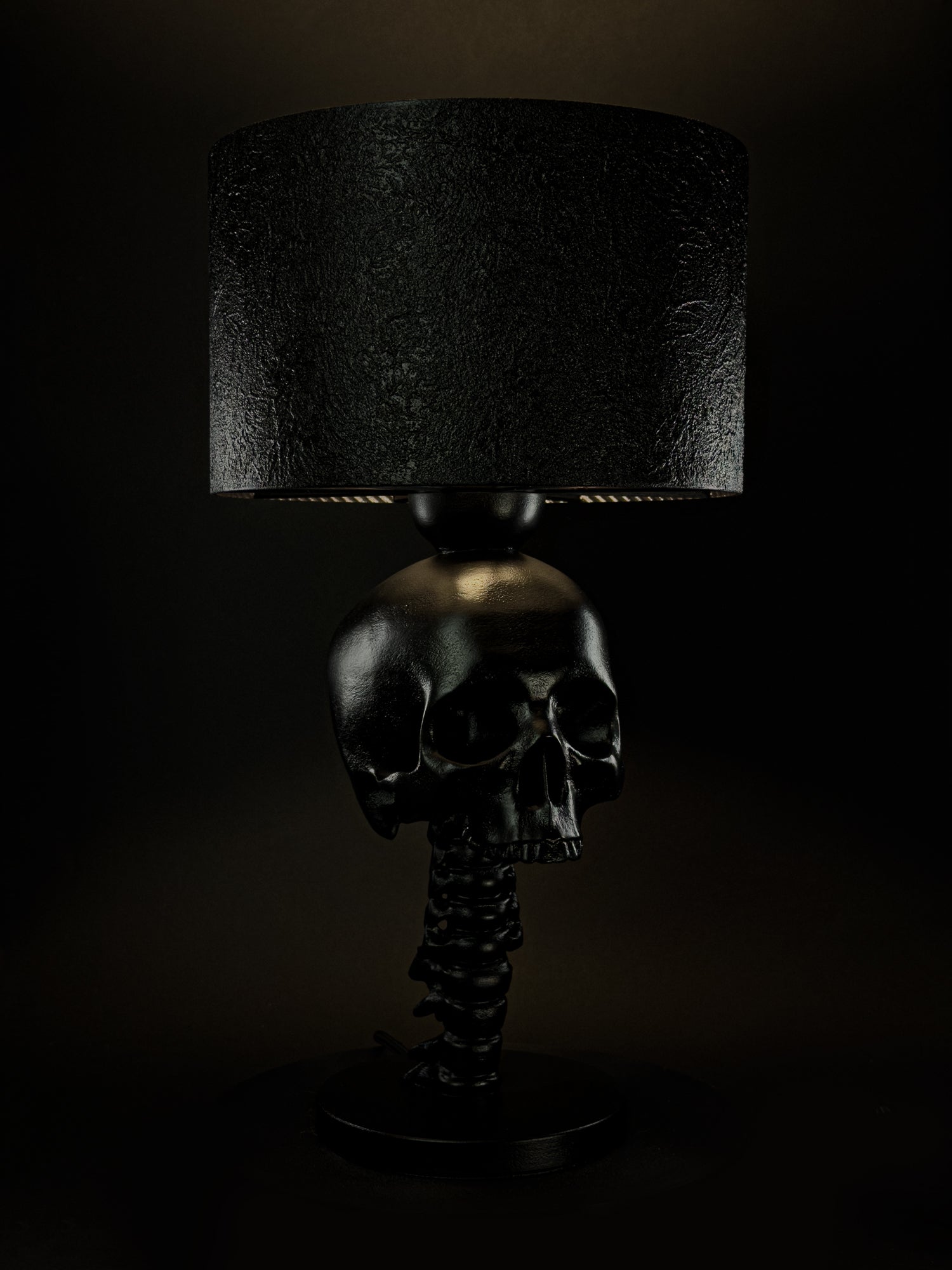 Illuminated black Skull Spine sculptural lamp shown from a three-quarter side angle
