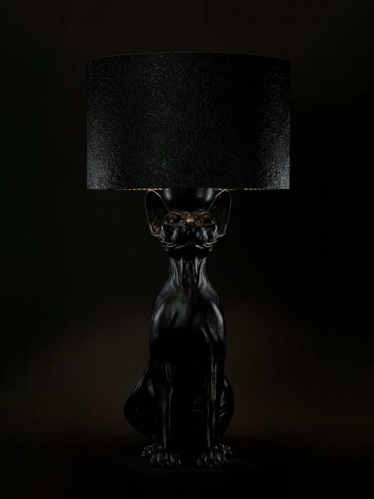 Front view of The Watcher black Sphynx cat table lamp with a textured drum shade.