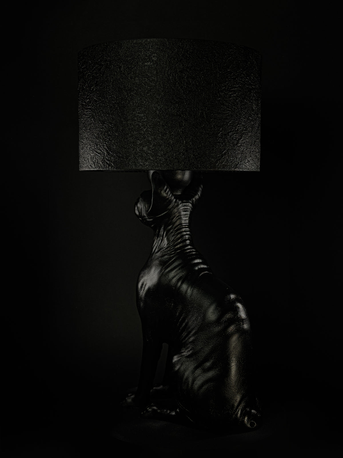 Rear three-quarter view of The Watcher black Sphynx cat lamp beneath its textured shade.