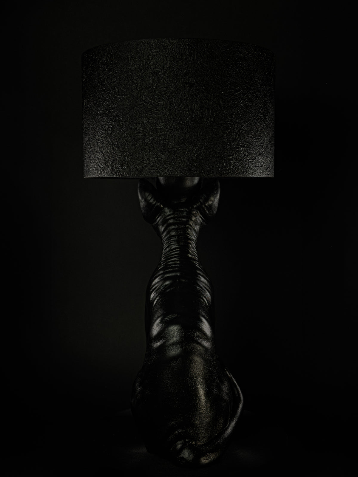 Back view of The Watcher black Sphynx cat lamp, showing folded skin and its curled tail.