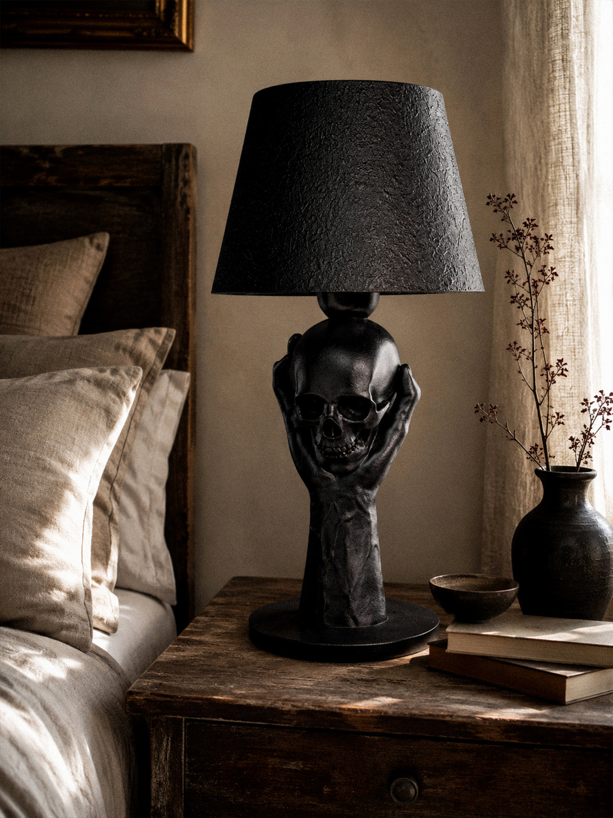 To Be or Not To Be black skull and hand table lamp on a rustic wooden bedside table beside books and a vase.