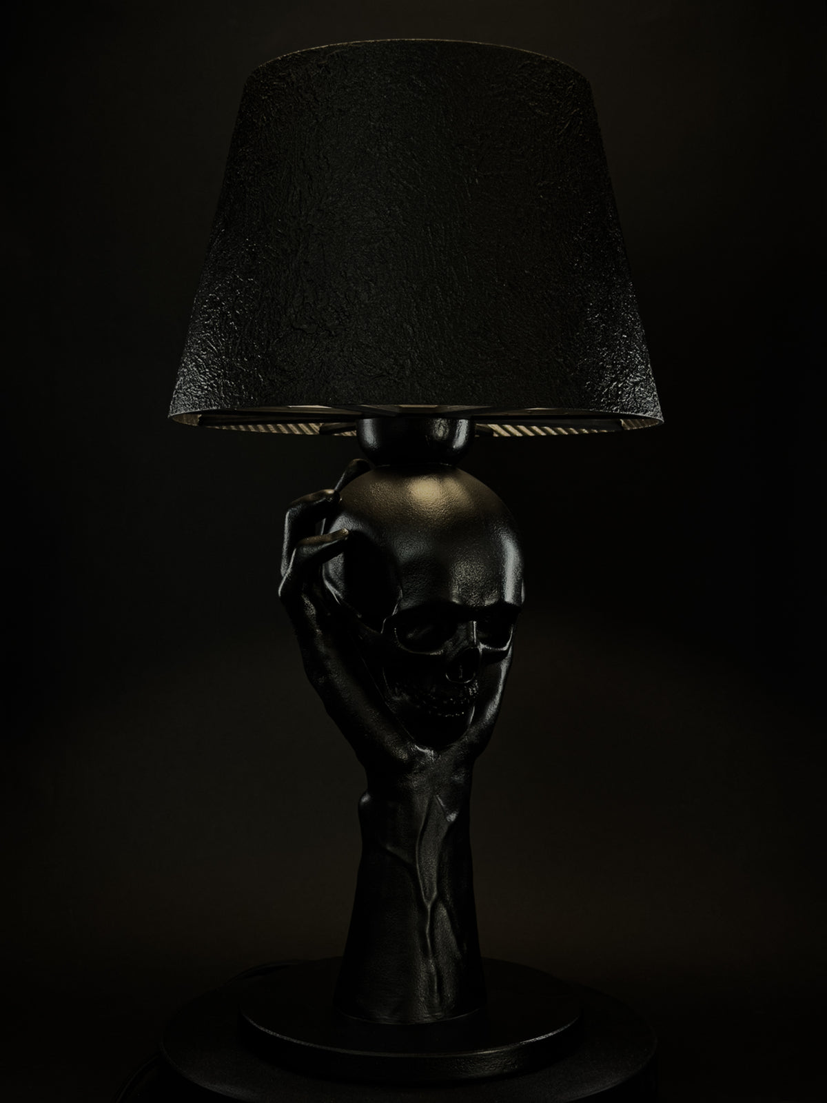 Three-quarter view of To Be or Not To Be, a black hand holding a skull beneath a textured lampshade.