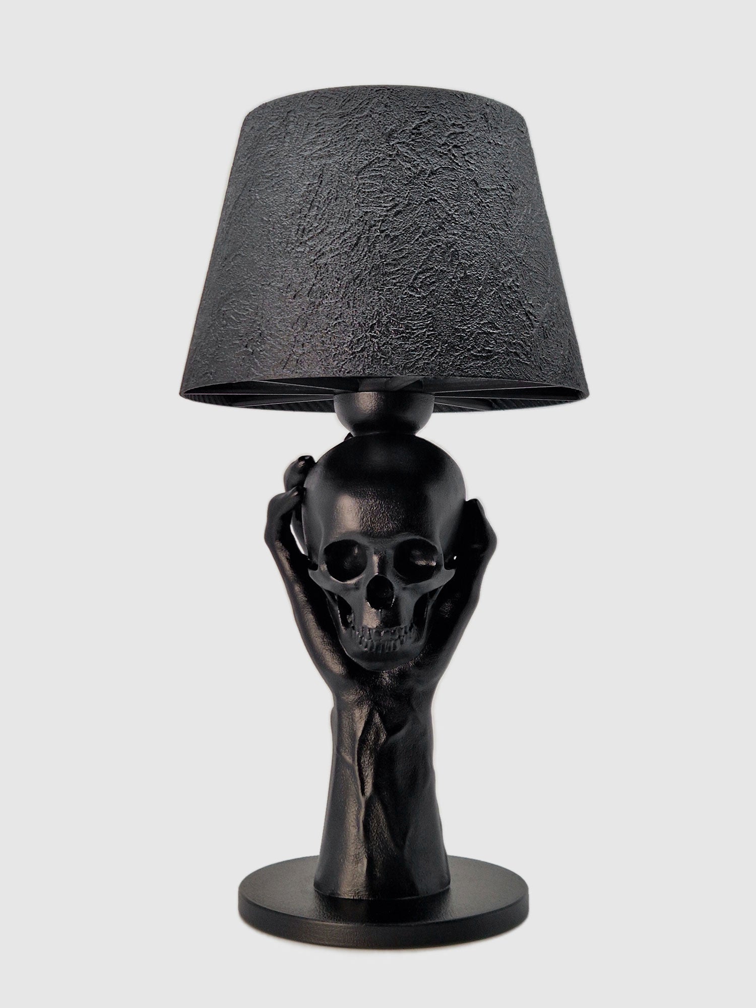 Front view of the 'To Be or Not To Be' lamp: a matte black hand holding a realistic skull with a black textured shade, original design by Horror Romance