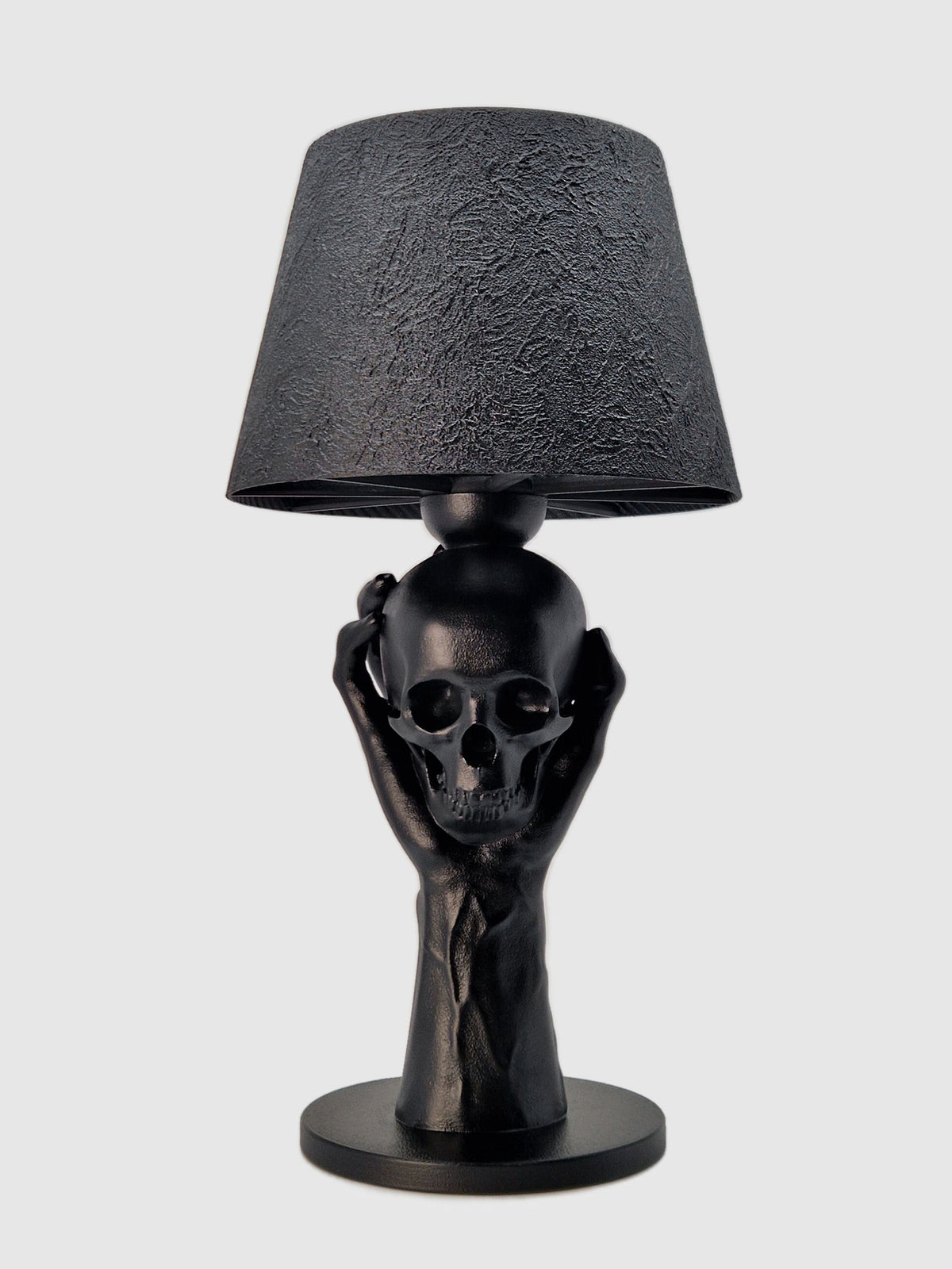 Front view of the 'To Be or Not To Be' lamp: a matte black hand holding a realistic skull with a black textured shade.