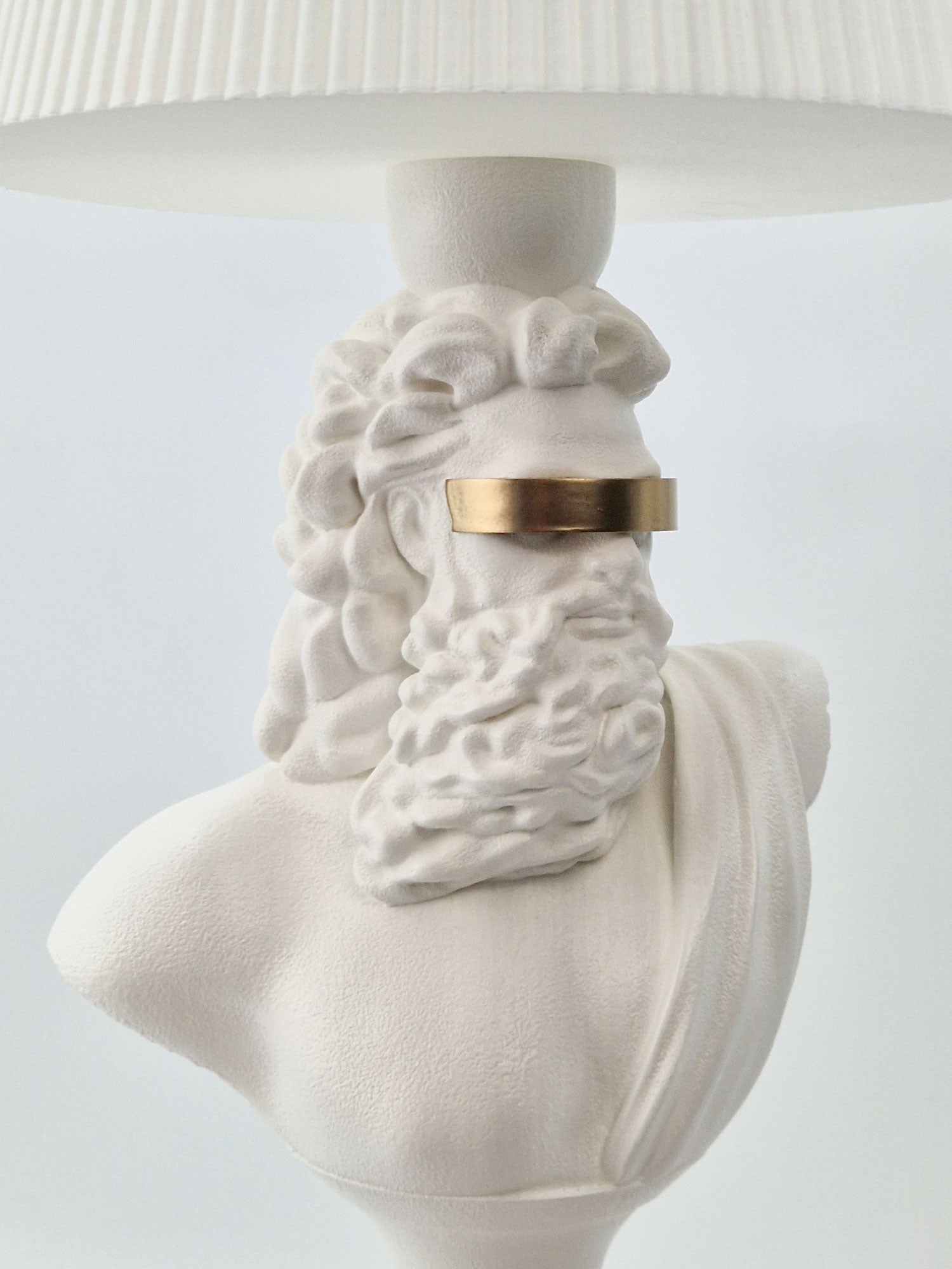 Close-up side view of the Zeus bust lamp showing the smooth matte white finish and metallic gold accent.