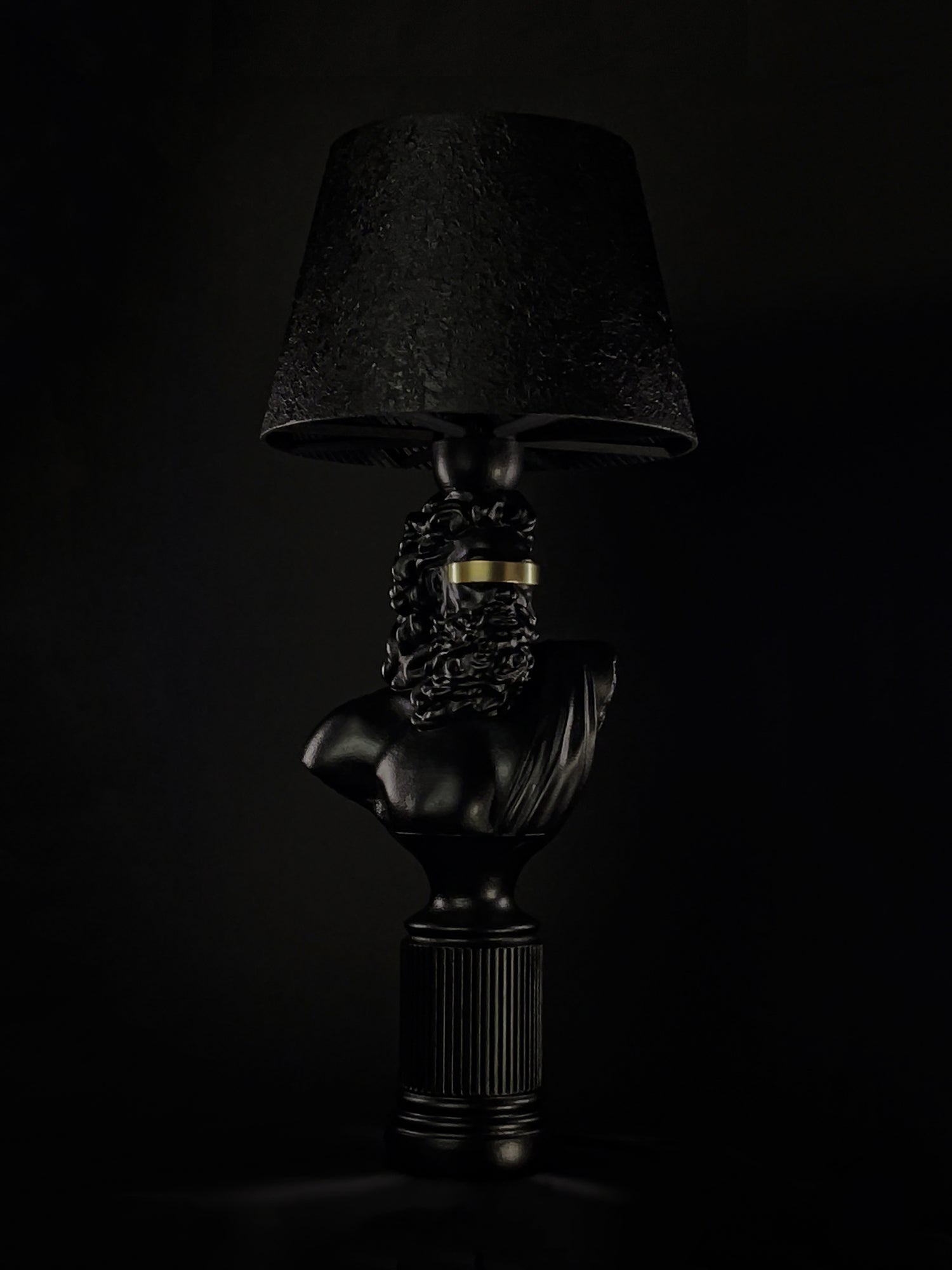 Three-quarter view of the satin-black Blind Zeus bust lamp with metallic-gold blindfold
