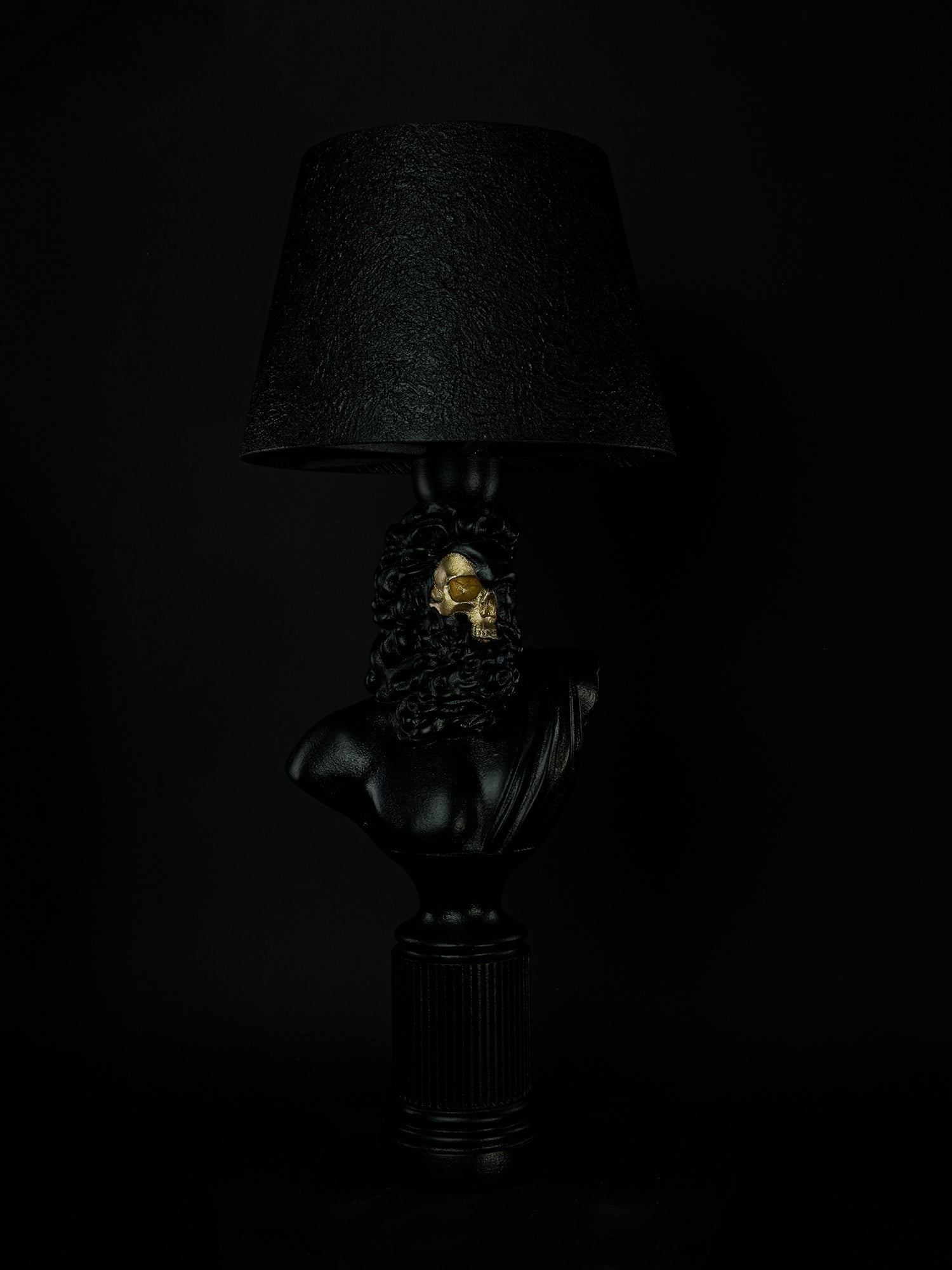 Three-quarter side view of the satin-black Zeus sculptural lamp with exposed gold skull