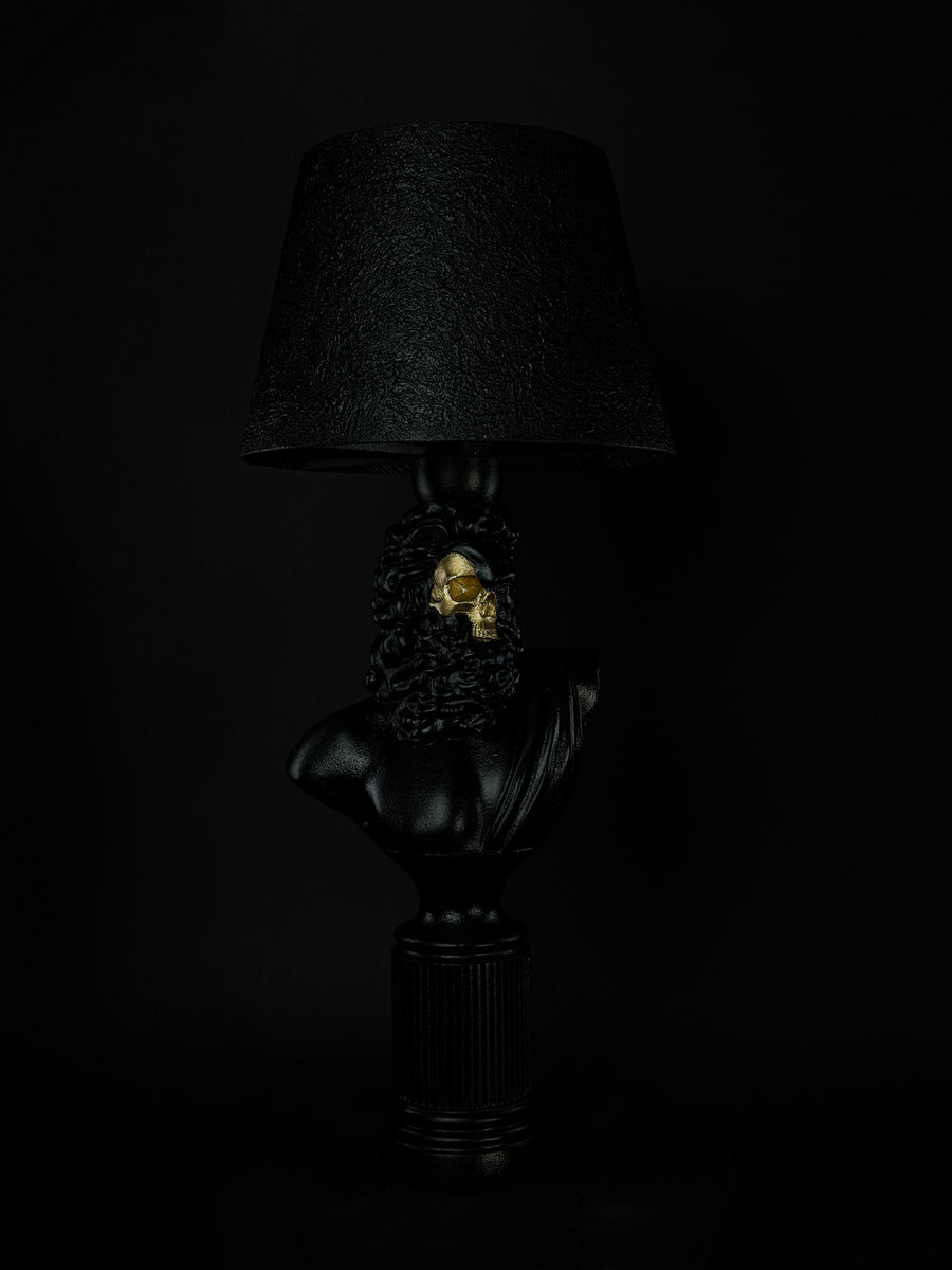 Three-quarter side view of the satin-black Zeus sculptural lamp with exposed gold skull